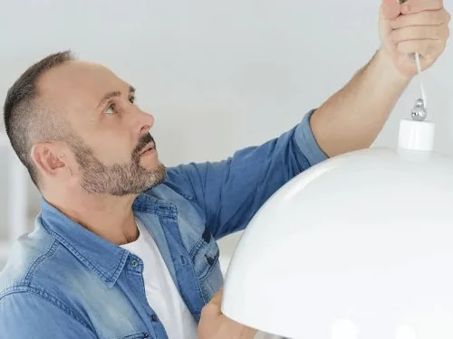 Mann hängt eine Lampe an die Decke