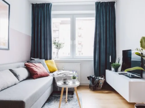 Kleines Wohnzimmer mit hellem Sofa, Beistelltisch und dunkelblauen Vorhängen