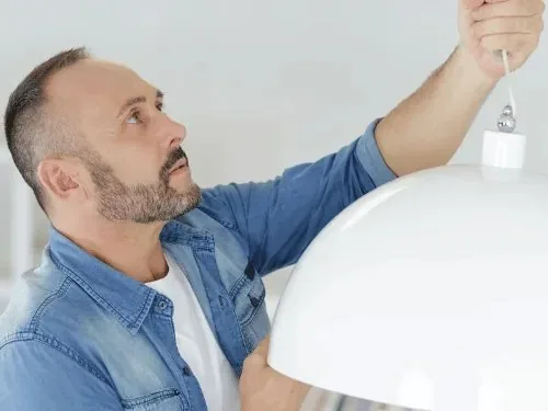 Mann hängt eine Deckenlampe auf
