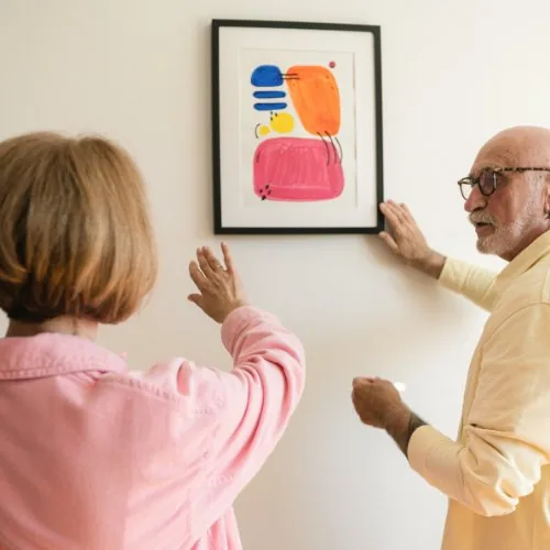 Älteres Paar hängt ein Bild an eine tapezierte Wand