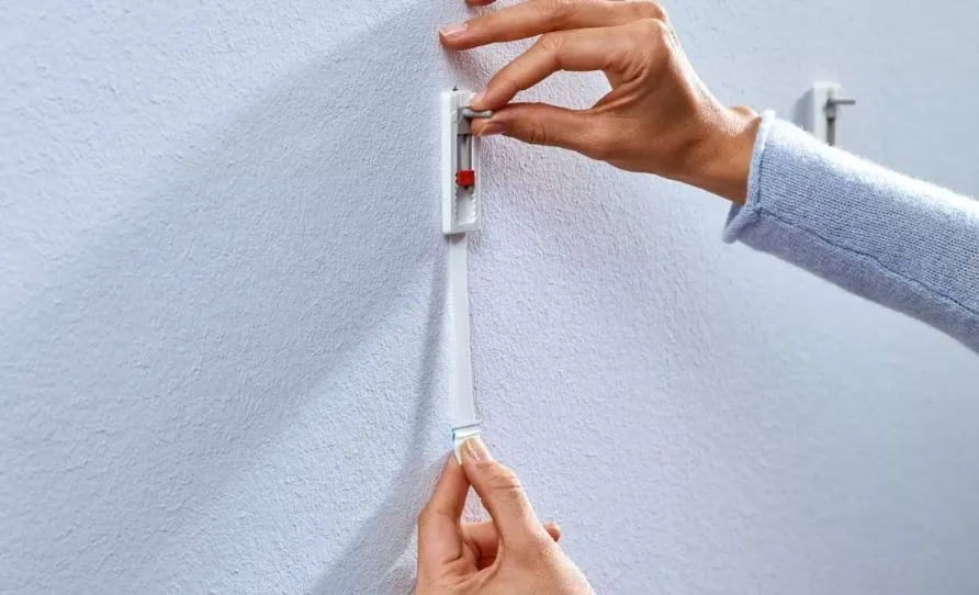Tesa Klebeschraube entfernen: Lasche flach an der Wand nach unten ziehen